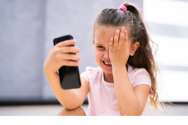 little girl holding one eye shut and focusing on a phone screen